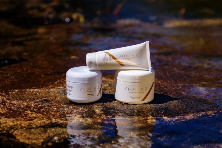 Pack para proteger la piel durante el verano con crema protectora, crema facial y crema corporal de cosméticos Siolaz, sobre una roca a la orilla del río.